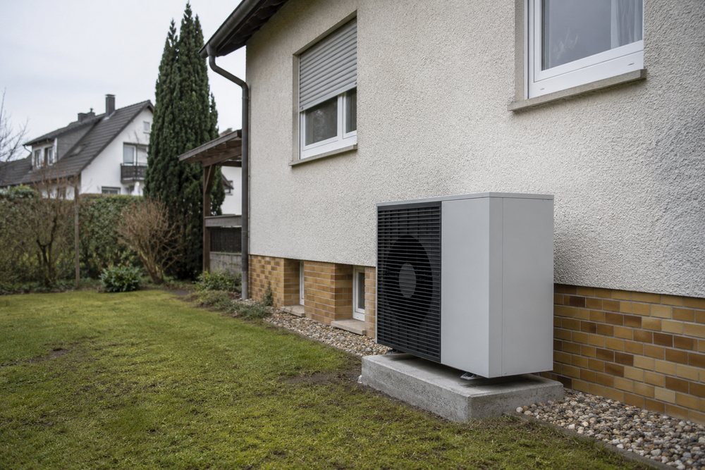 Eine Wärmepumpen-Außeneinheit auf einem Betonsockel neben der Hauswand eines Einfamilienhauses.